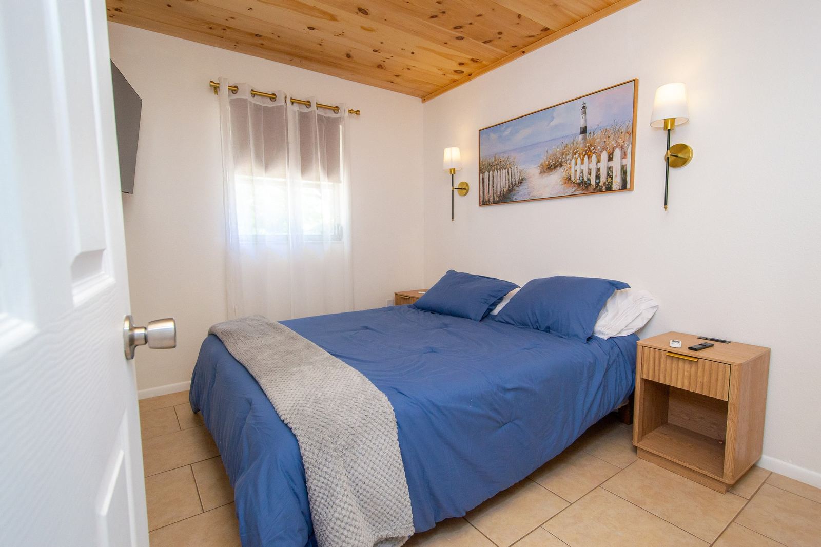 Queen bedroom with pine ceiling and coastal lighthouse art